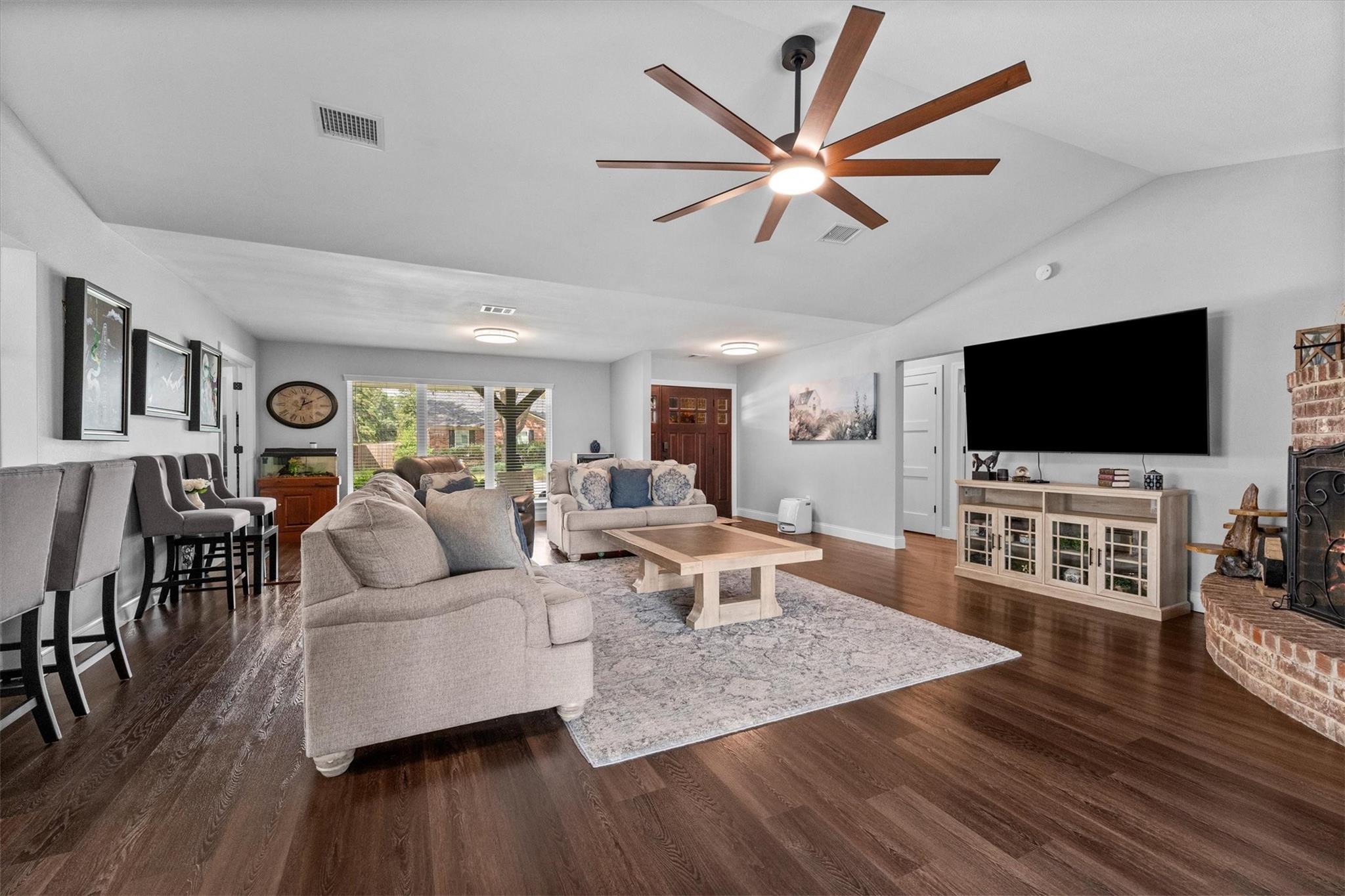 Furnished living room with dark wood floors, gray sofas, a large ceiling fan, and a brick fireplace.