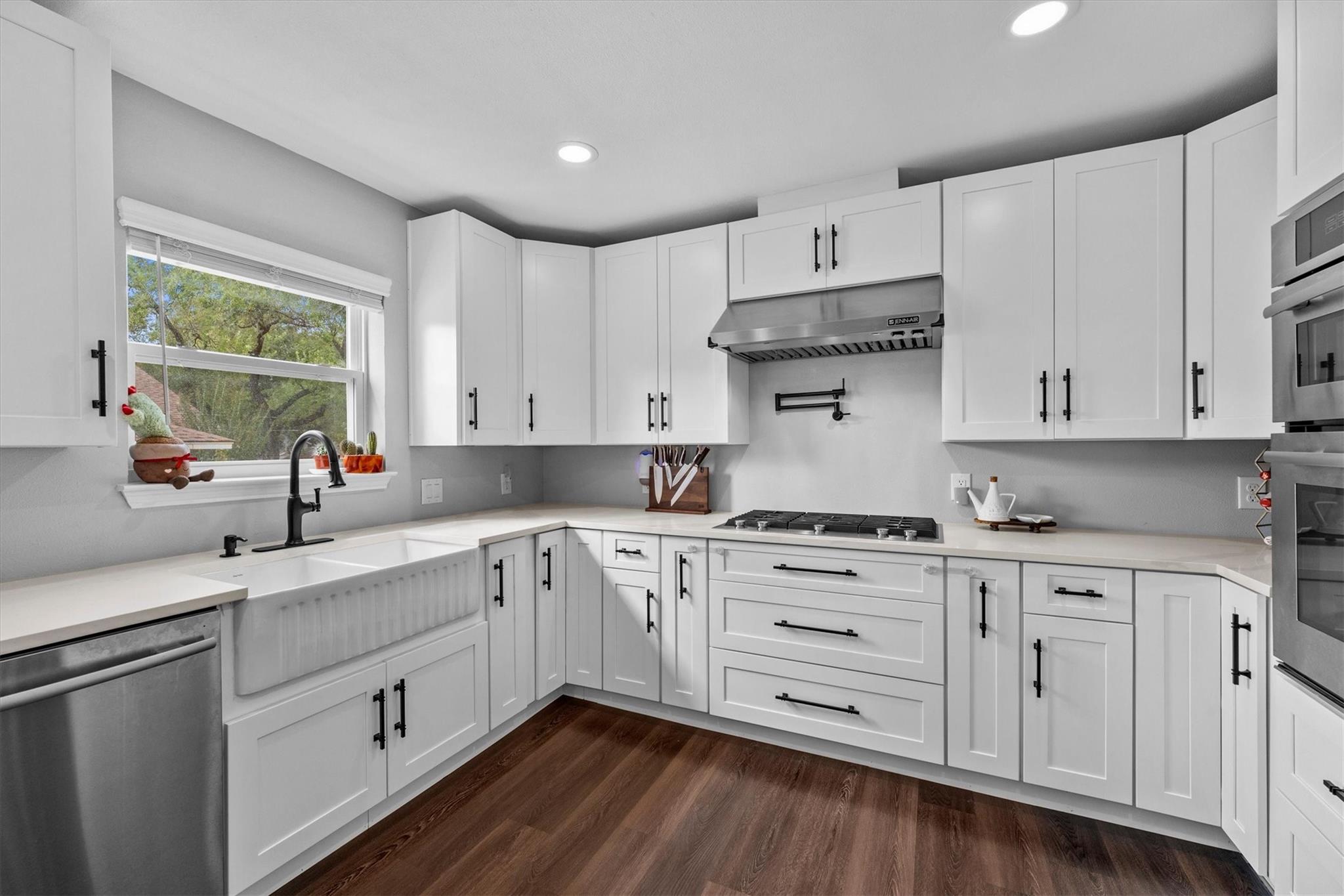Bright white kitchen with shaker cabinets, farmhouse sink, gas cooktop, and dark wood flooring.