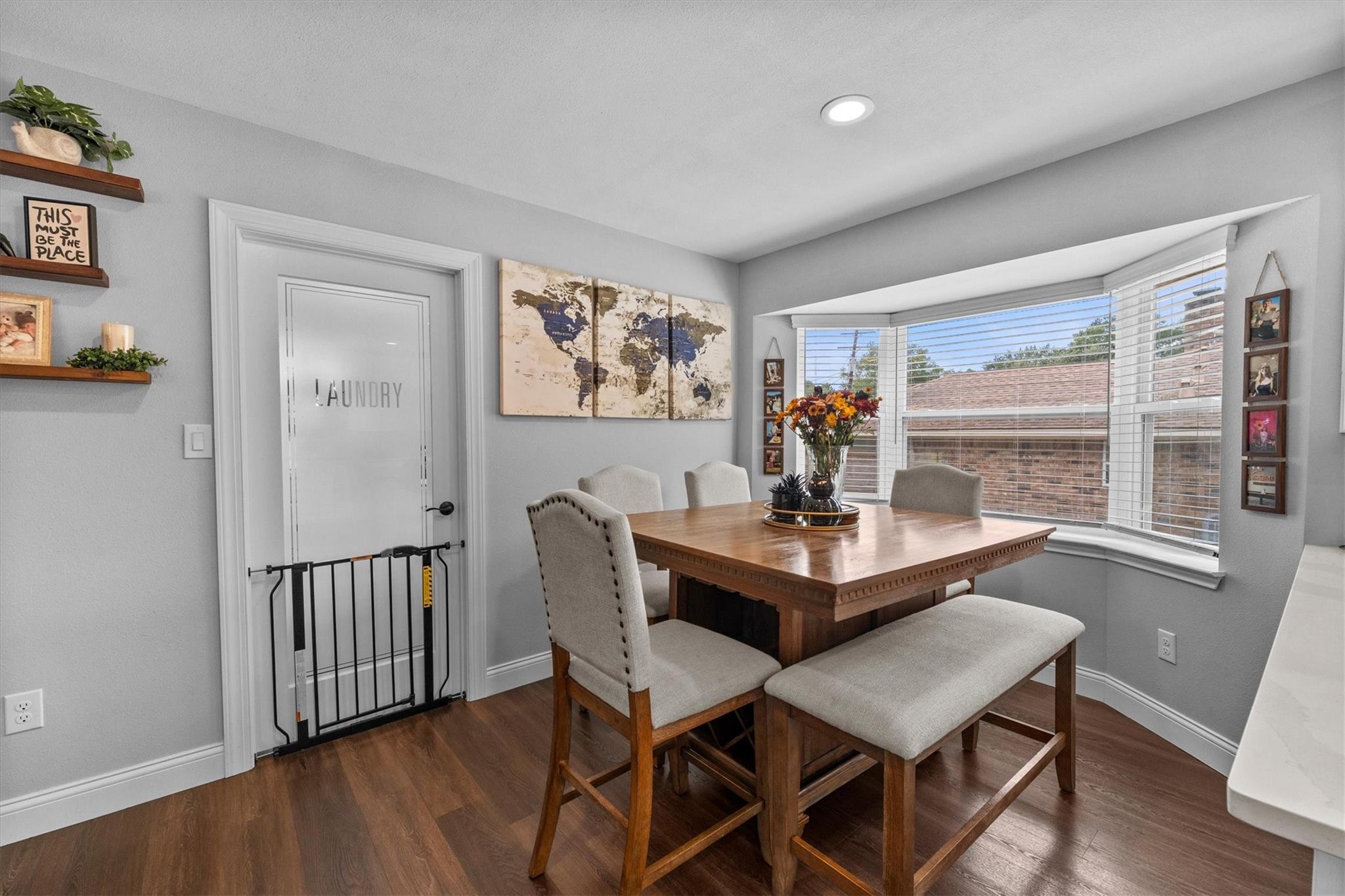 Dining area with a wooden table and bench beside a large bay window; laundry door has a safety gate.