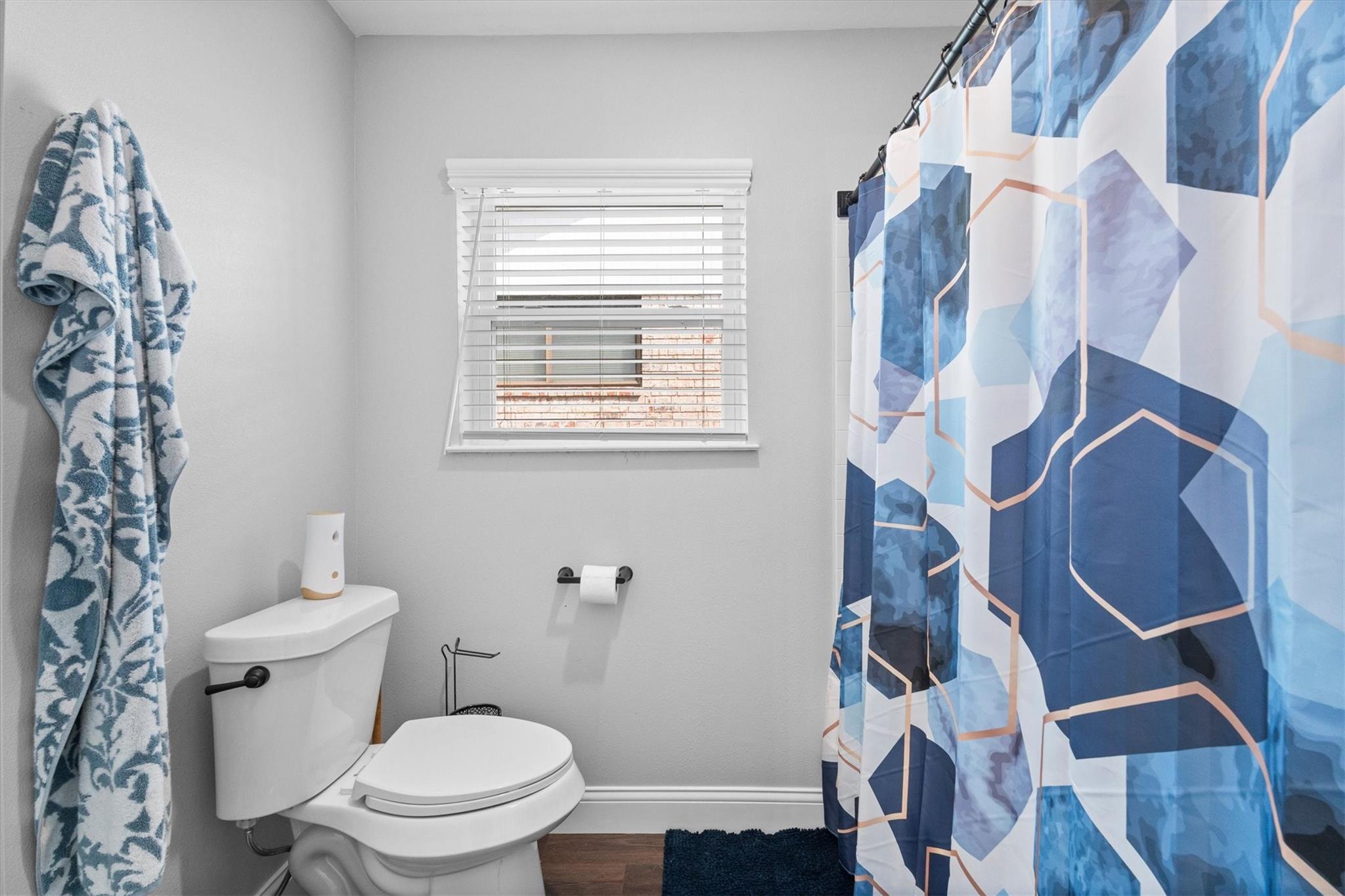 Bathroom with a blue geometric shower curtain, patterned towel, and window above the toilet.