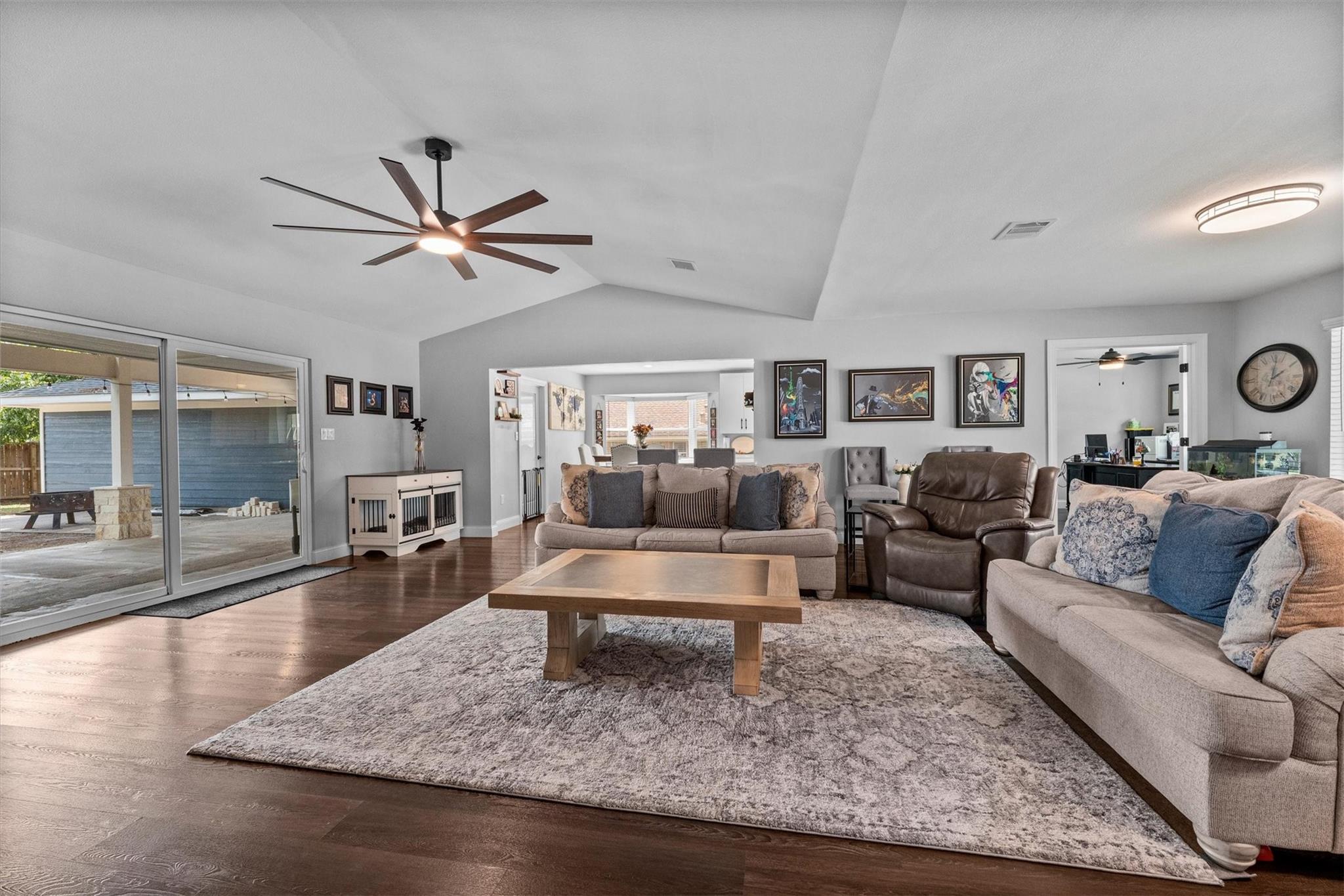 Living room with vaulted ceiling, wood floors, sofas, and sliding glass doors to a covered patio.