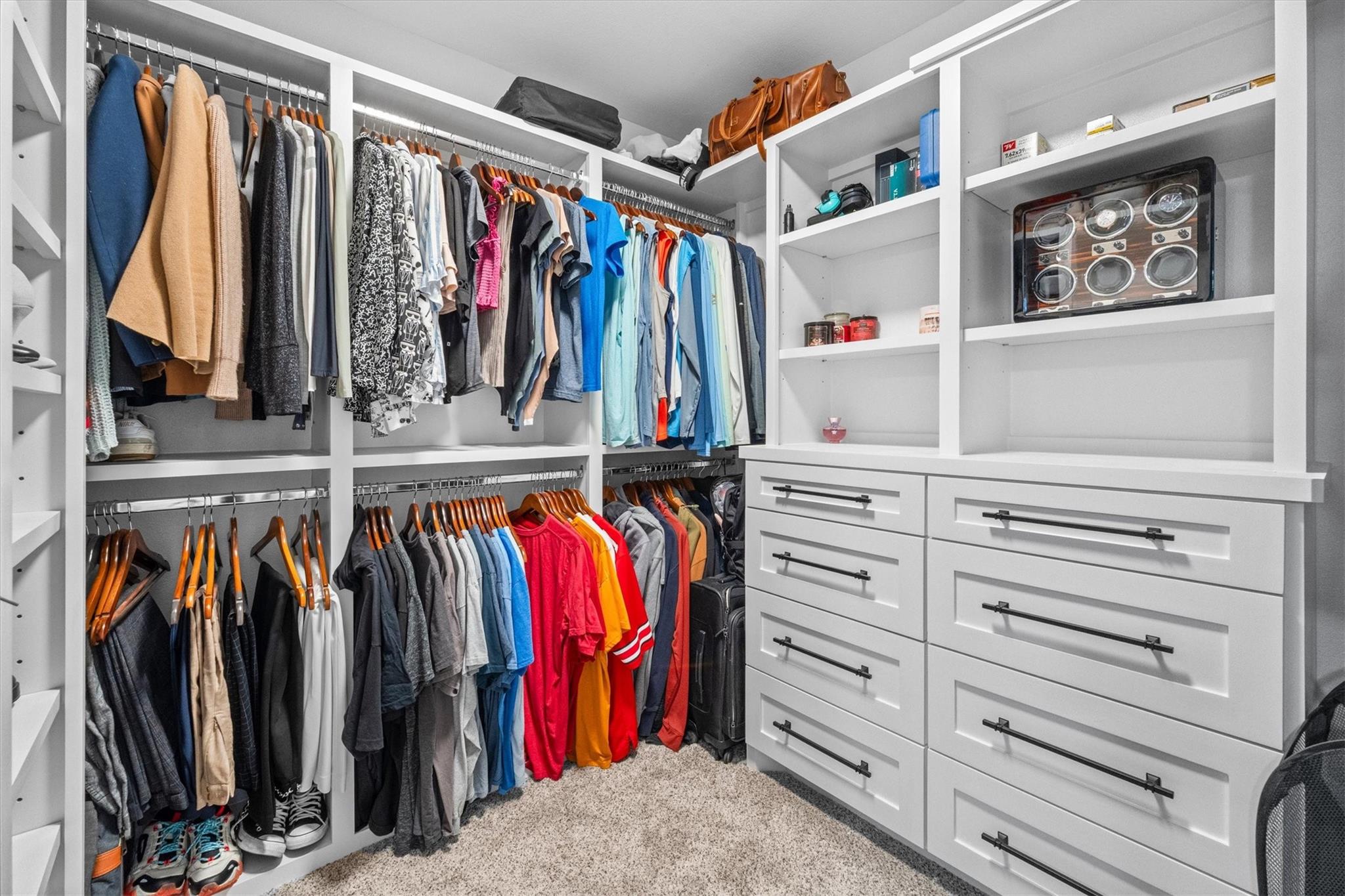 Walk-in closet with built-in white drawers, extensive clothing racks, and a watch display case.