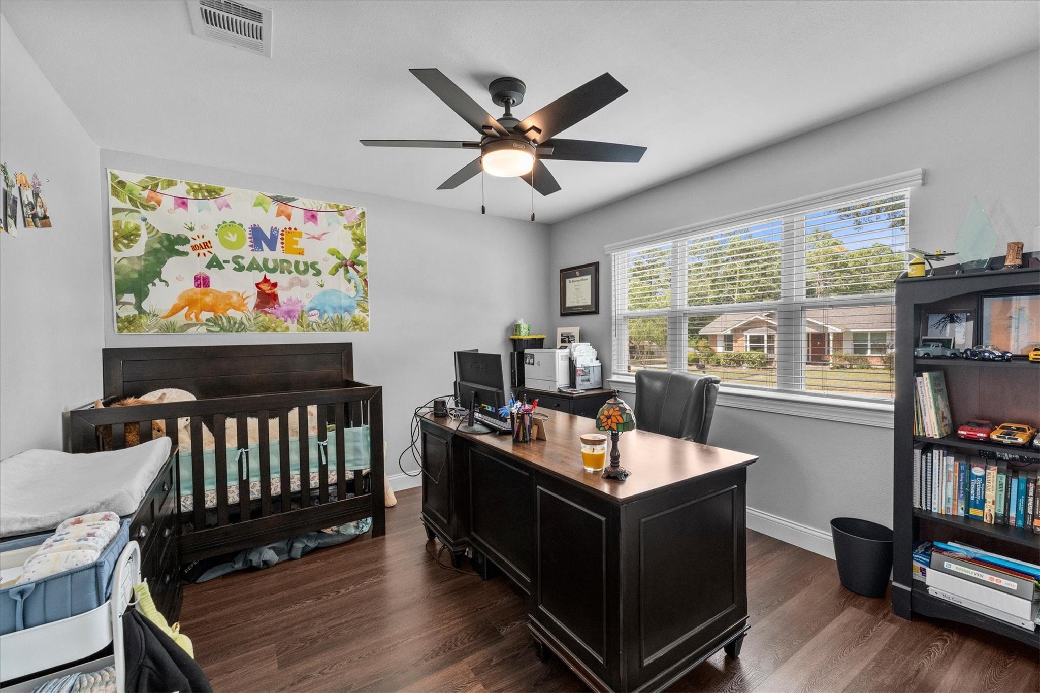 Home office and nursery with a dark wood crib, executive desk, and dinosaur banner.