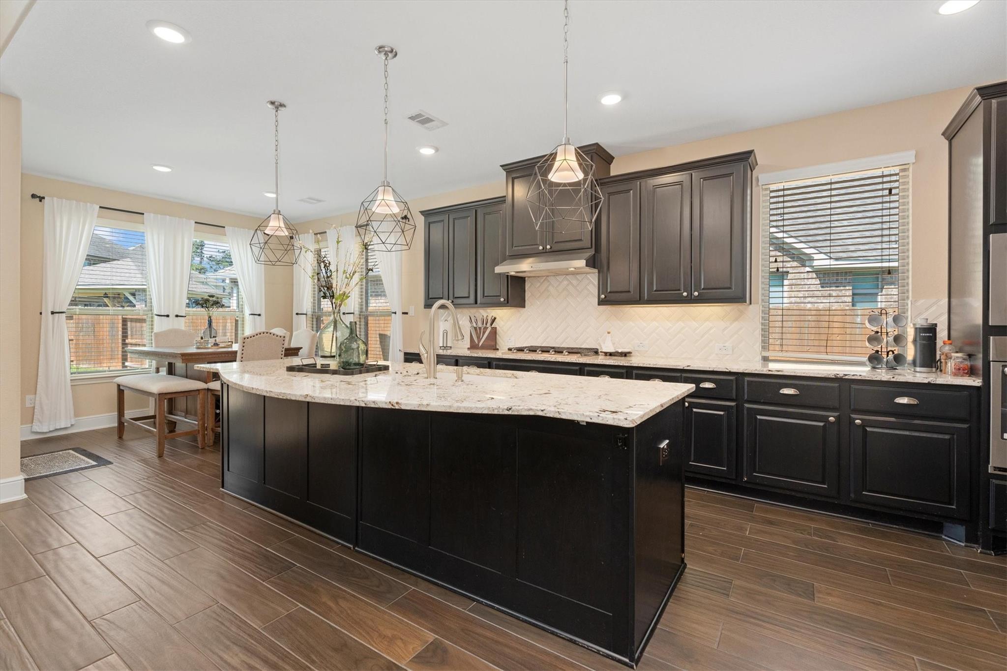Kitchen with dark cabinets, a large white stone island, geometric pendant lights, and an adjoining dining nook.