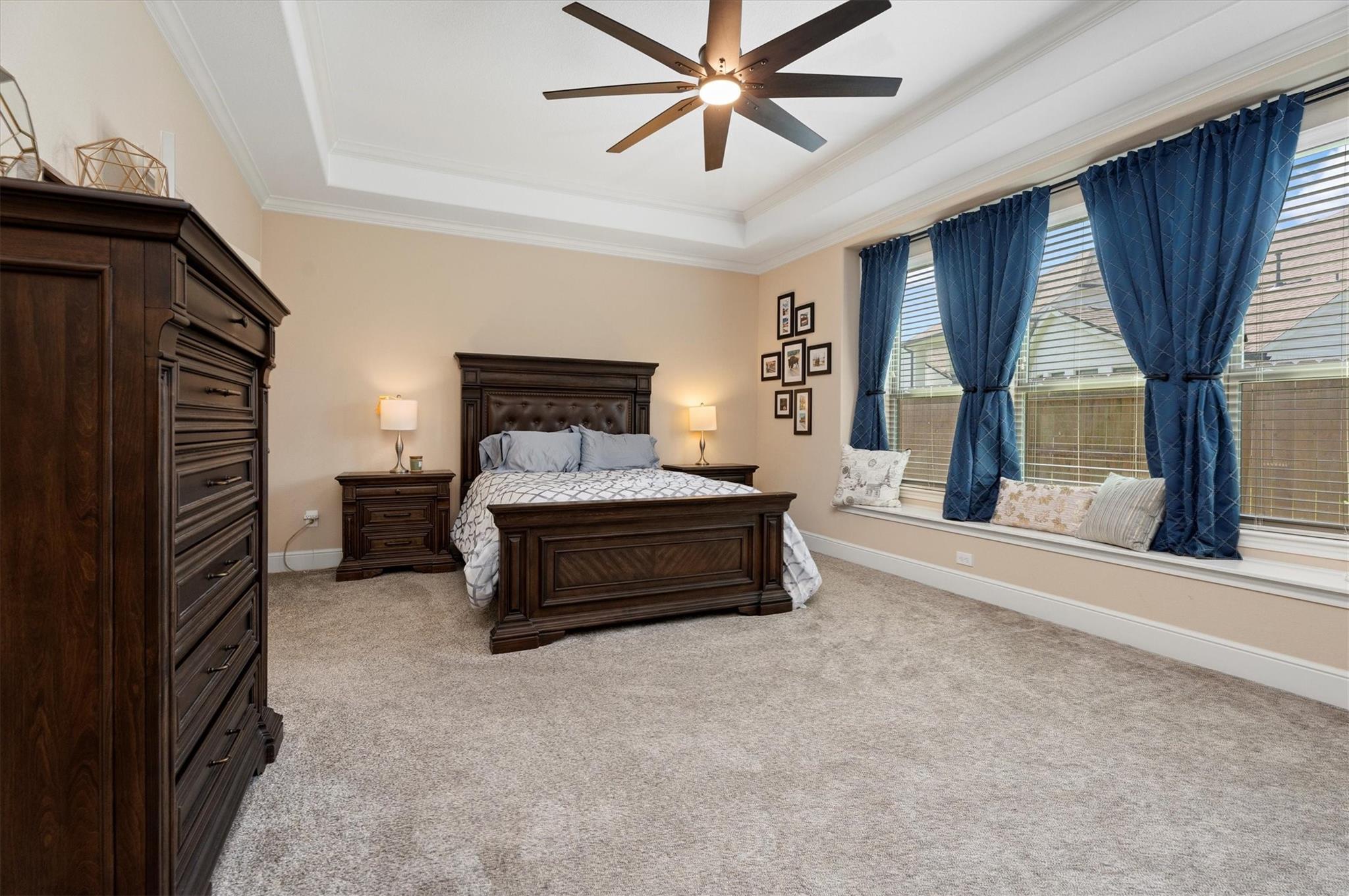 Furnished bedroom with dark wood bed, blue curtains, and a tray ceiling with a fan.