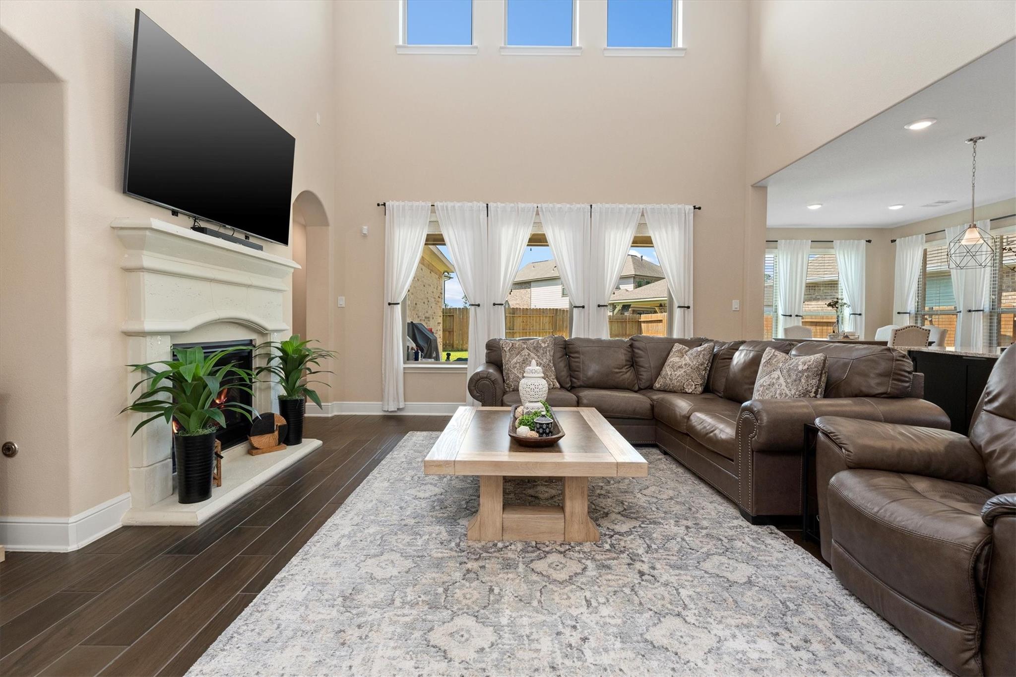 Living room with a vaulted ceiling, white fireplace, mounted television, and brown leather sectional.