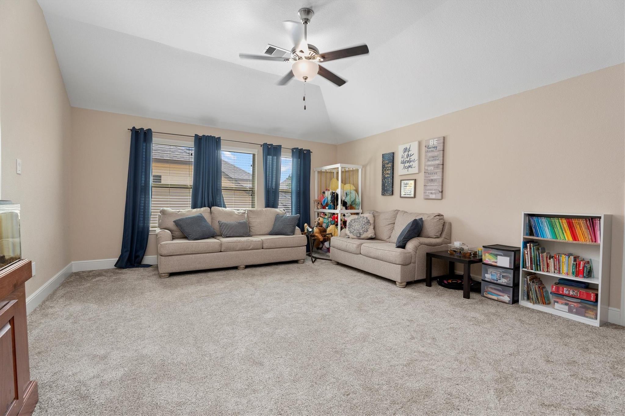 Furnished living room with beige sofas, blue curtains, plush carpet, and a ceiling fan.