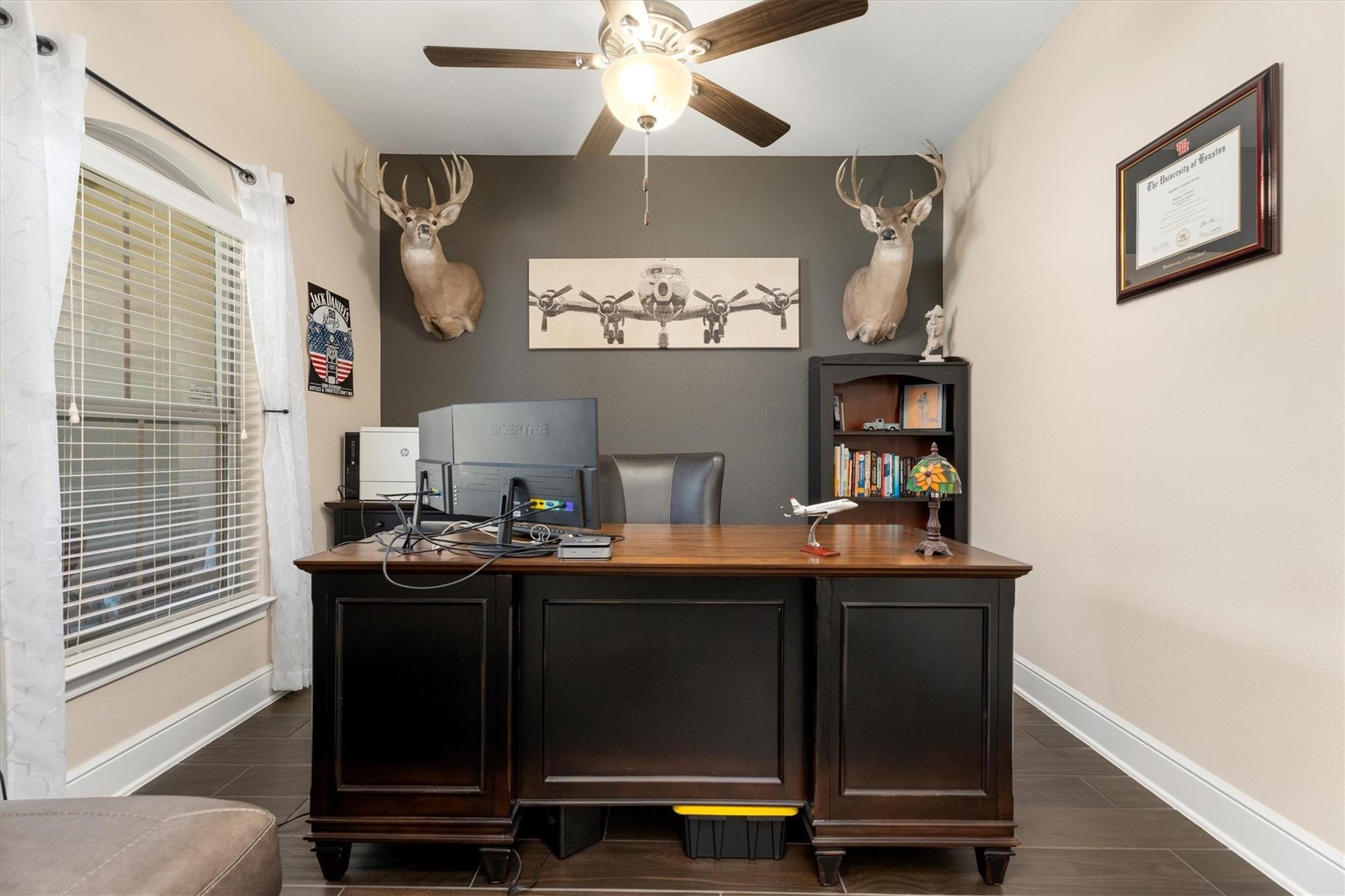 Furnished home office with a large dark wood desk, mounted deer heads, and airplane artwork.
