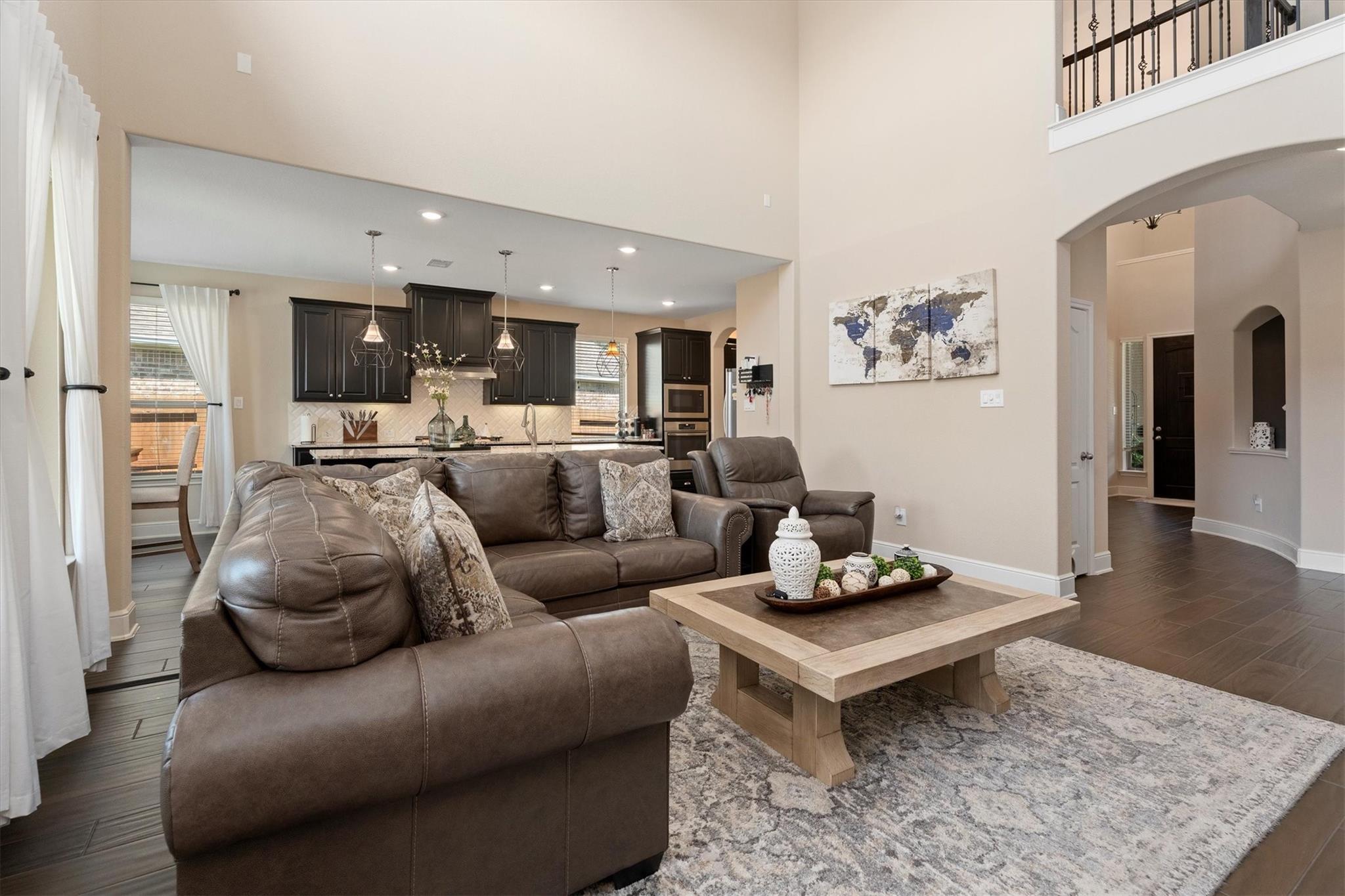 Living room with a brown leather sectional, light wood coffee table, and open kitchen behind it.