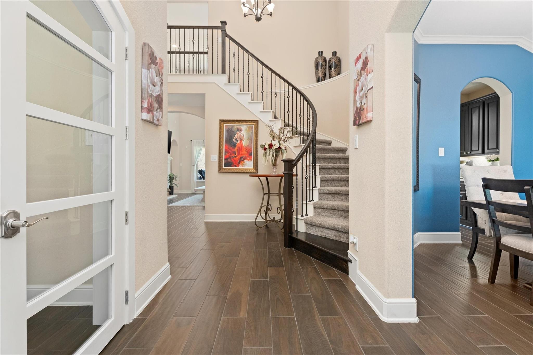 Entry foyer with a curved staircase, wood-look tile floors, and an adjoining blue dining area.