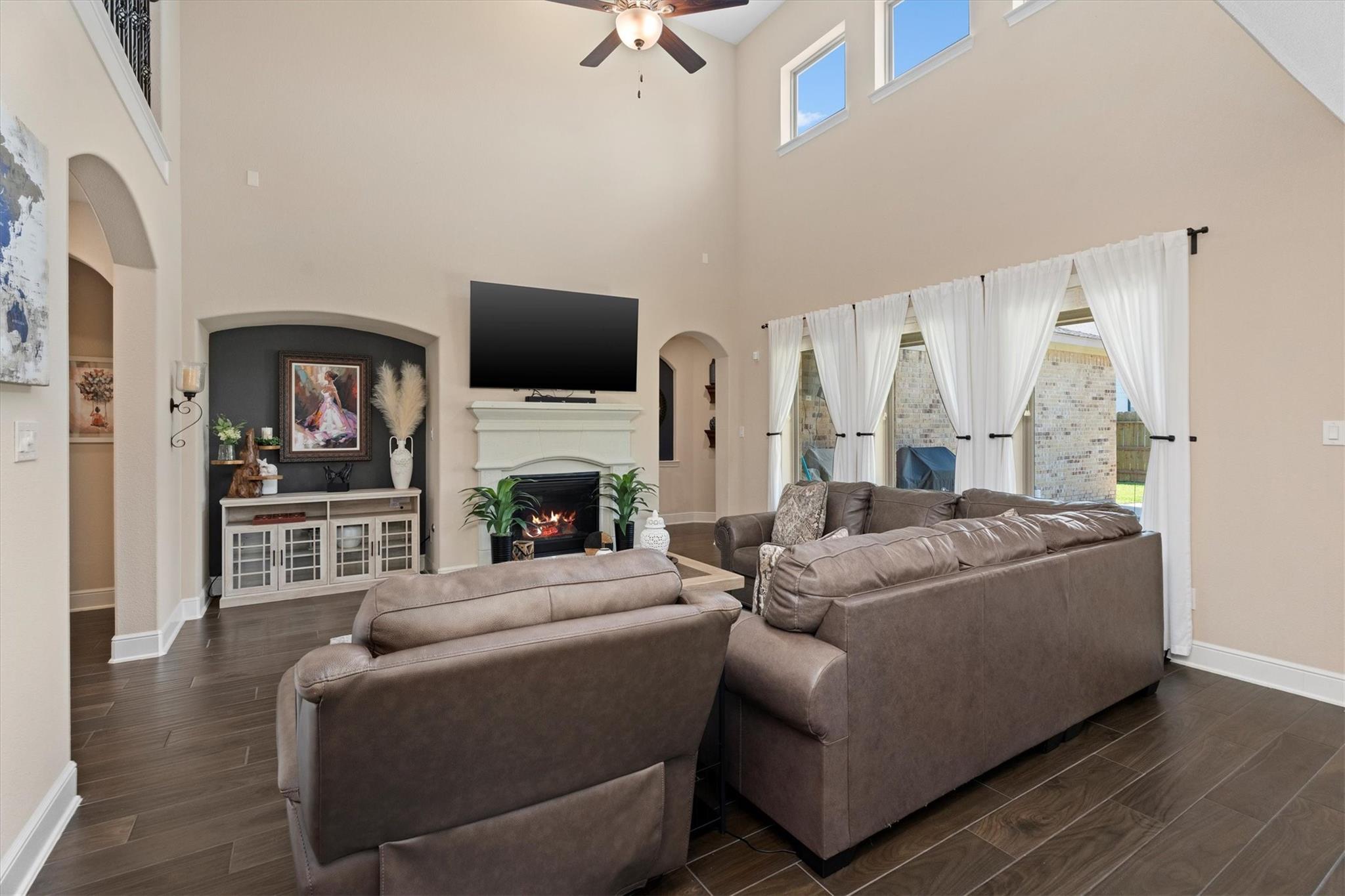 Double-height living room with taupe sectionals, a fireplace, and tall curtained windows.