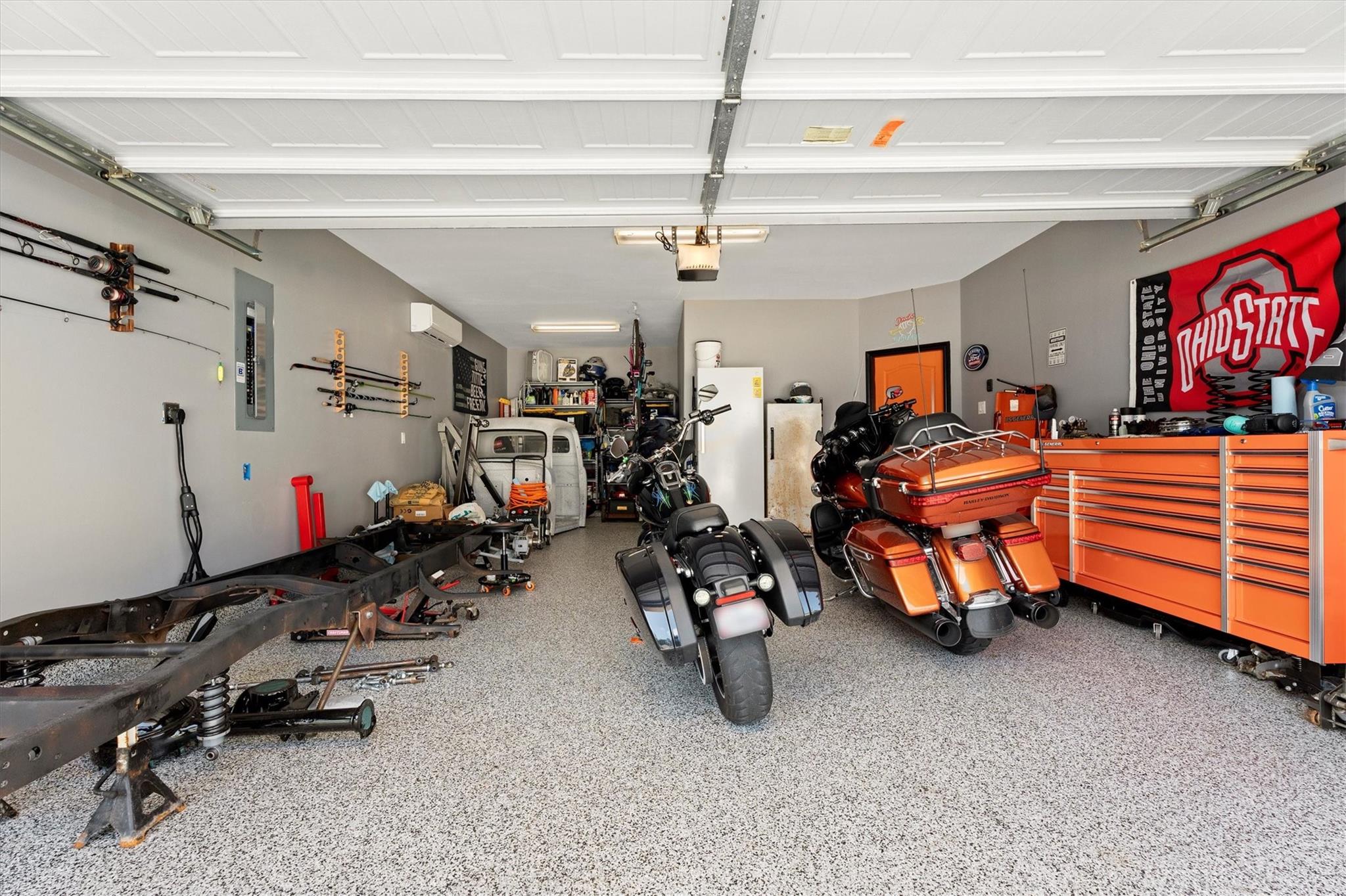 Garage with motorcycles, orange tool chests, wall-mounted fishing rods, and a speckled epoxy floor.