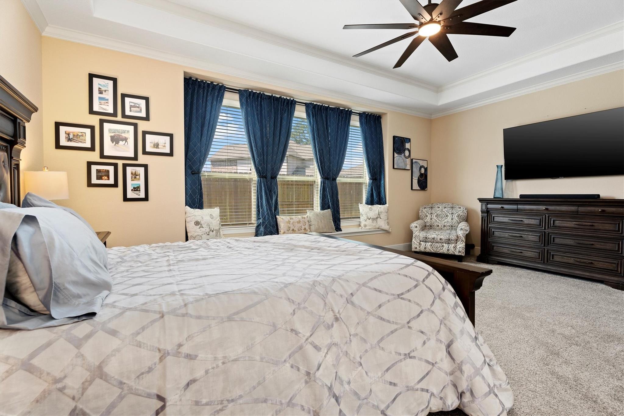 Furnished bedroom with a large bed, blue curtains, and a wall-mounted television.