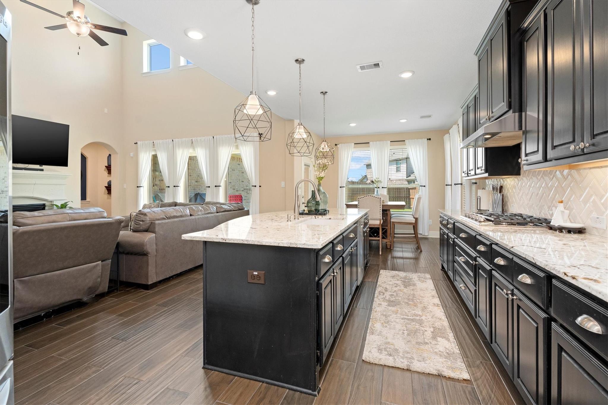 Open-plan kitchen with a large stone island, dark cabinets, and pendant lights beside the living room.