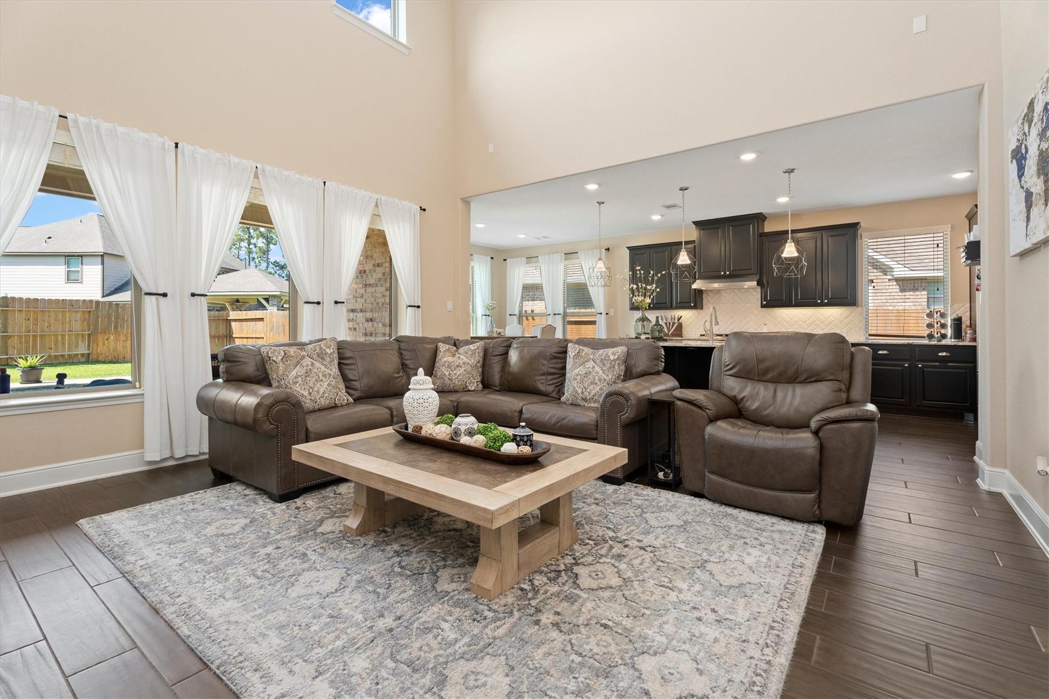 Living room with a leather sectional and recliner opening to a dark-cabinet kitchen.