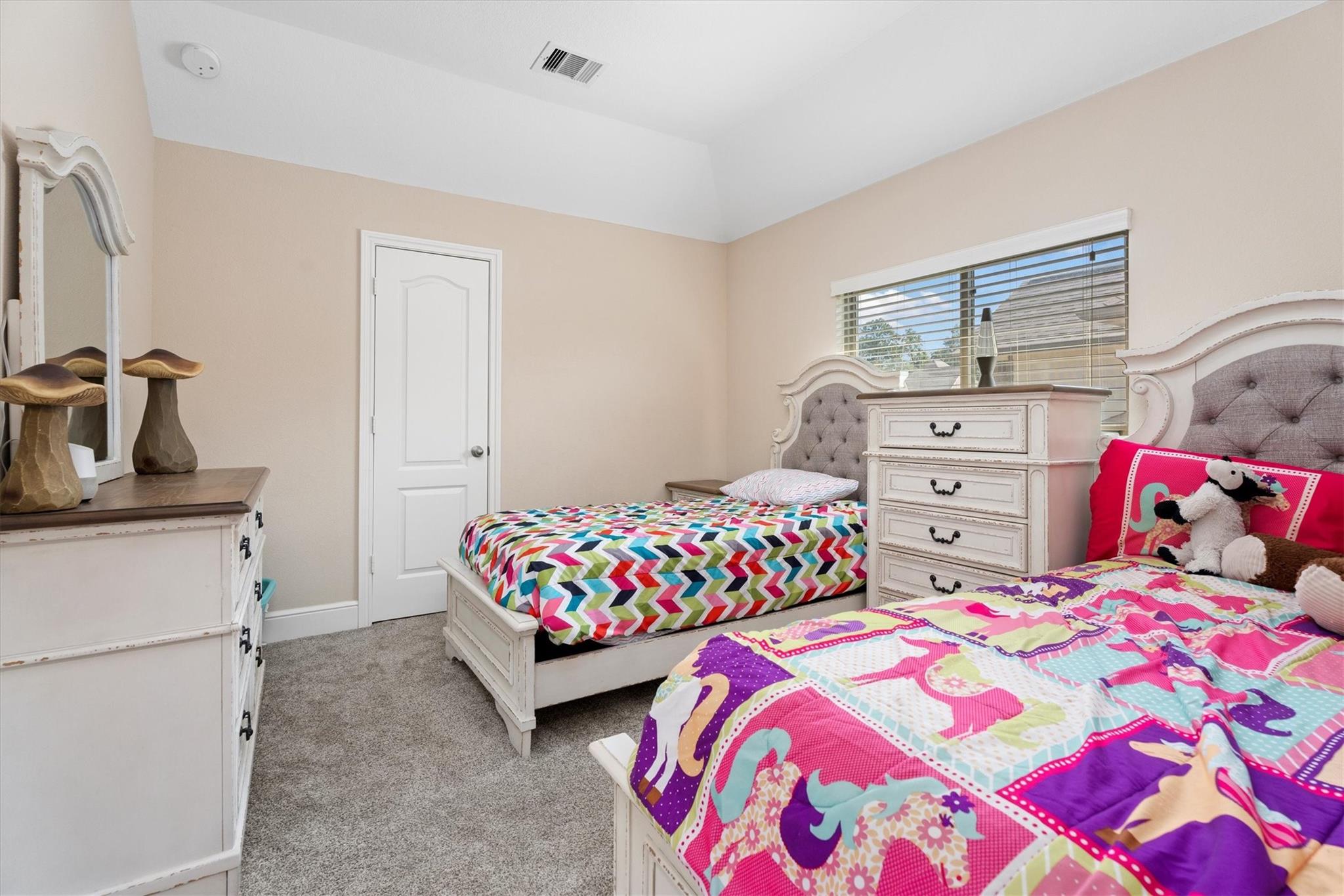 Bedroom with two white beds, colorful patterned bedding, and a white dresser.
