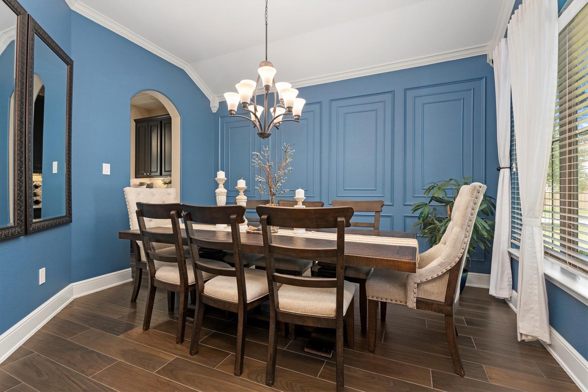 Dining room with blue paneled walls, a dark wood table, chandelier, and large curtained windows.
