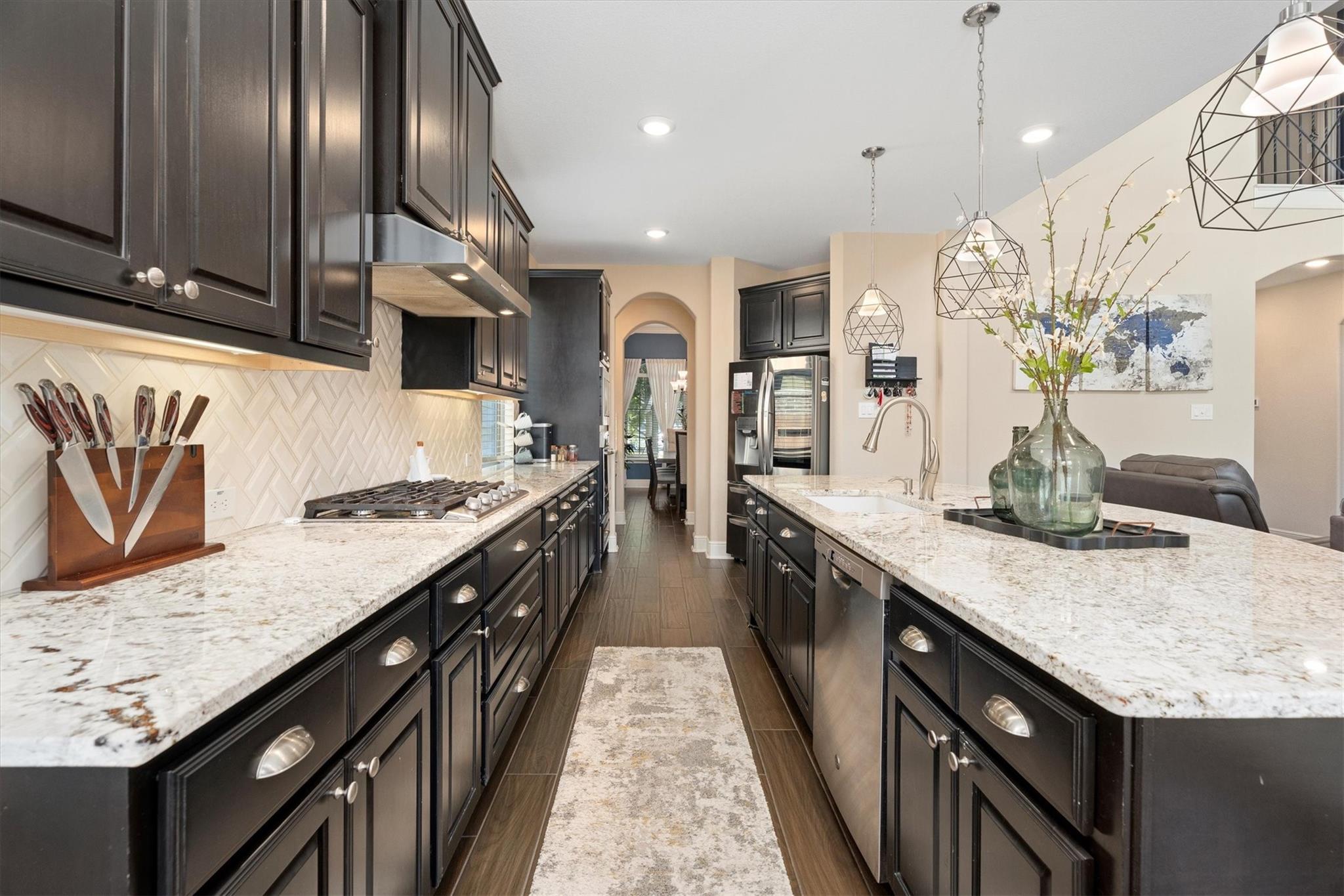 Kitchen with dark cabinets, granite countertops, stainless steel appliances, and a large island with a sink.