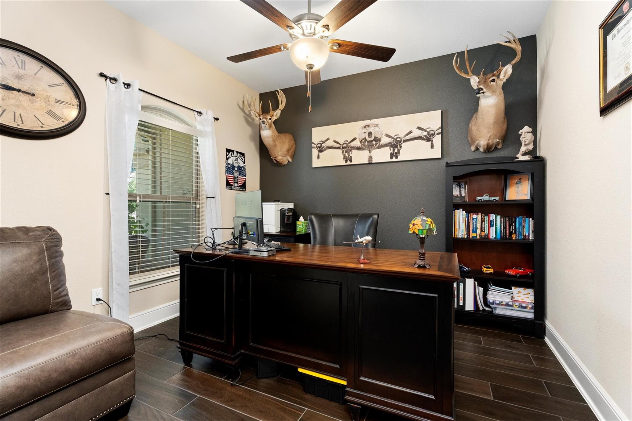Home office with a large wood desk, deer mounts, airplane artwork, and a bookcase.