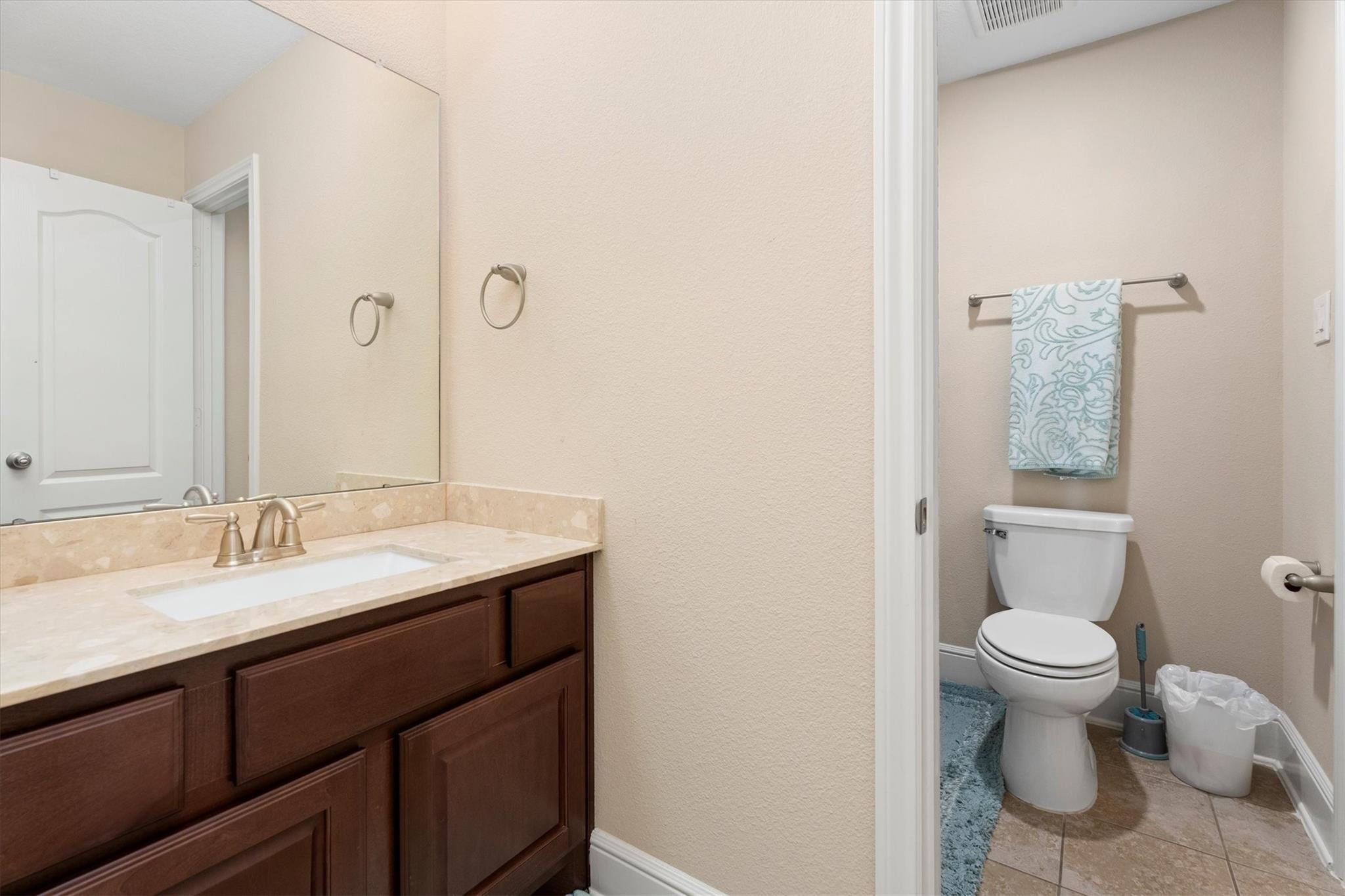 Bathroom with a dark wood vanity and mirror beside a separate toilet area with a patterned towel.
