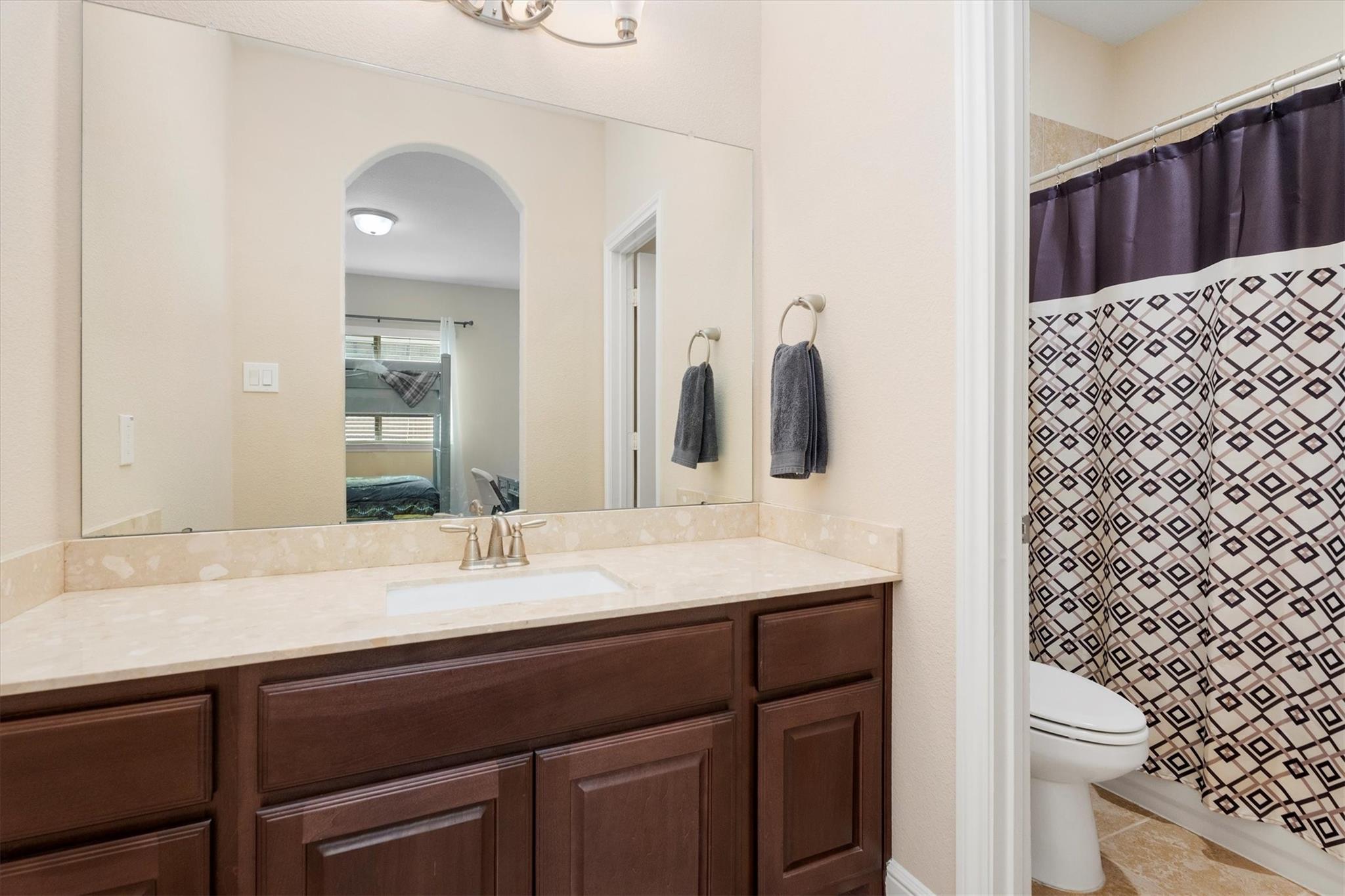 Bathroom with a dark wood vanity, wide mirror, and geometric-patterned shower curtain.