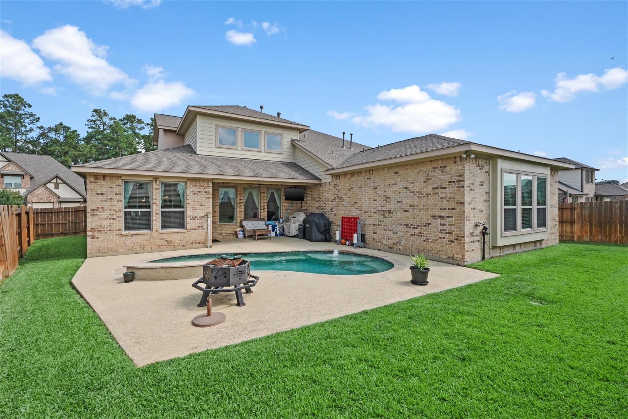 Brick home with a fenced backyard pool, broad patio, and green lawn.