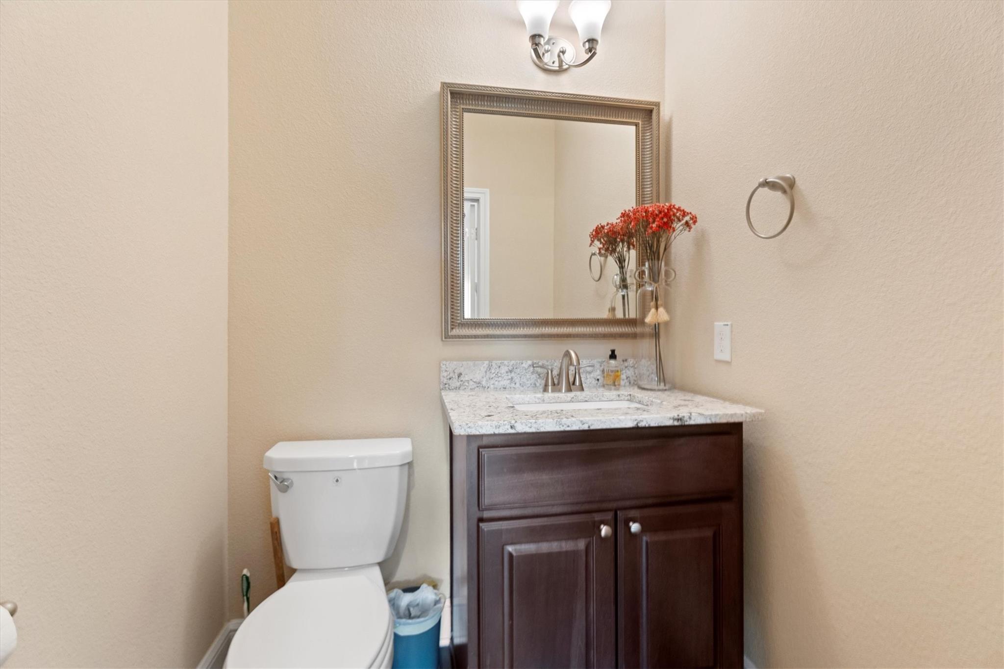 Bathroom vanity with a white-and-gray stone countertop, framed mirror, and toilet beside it.