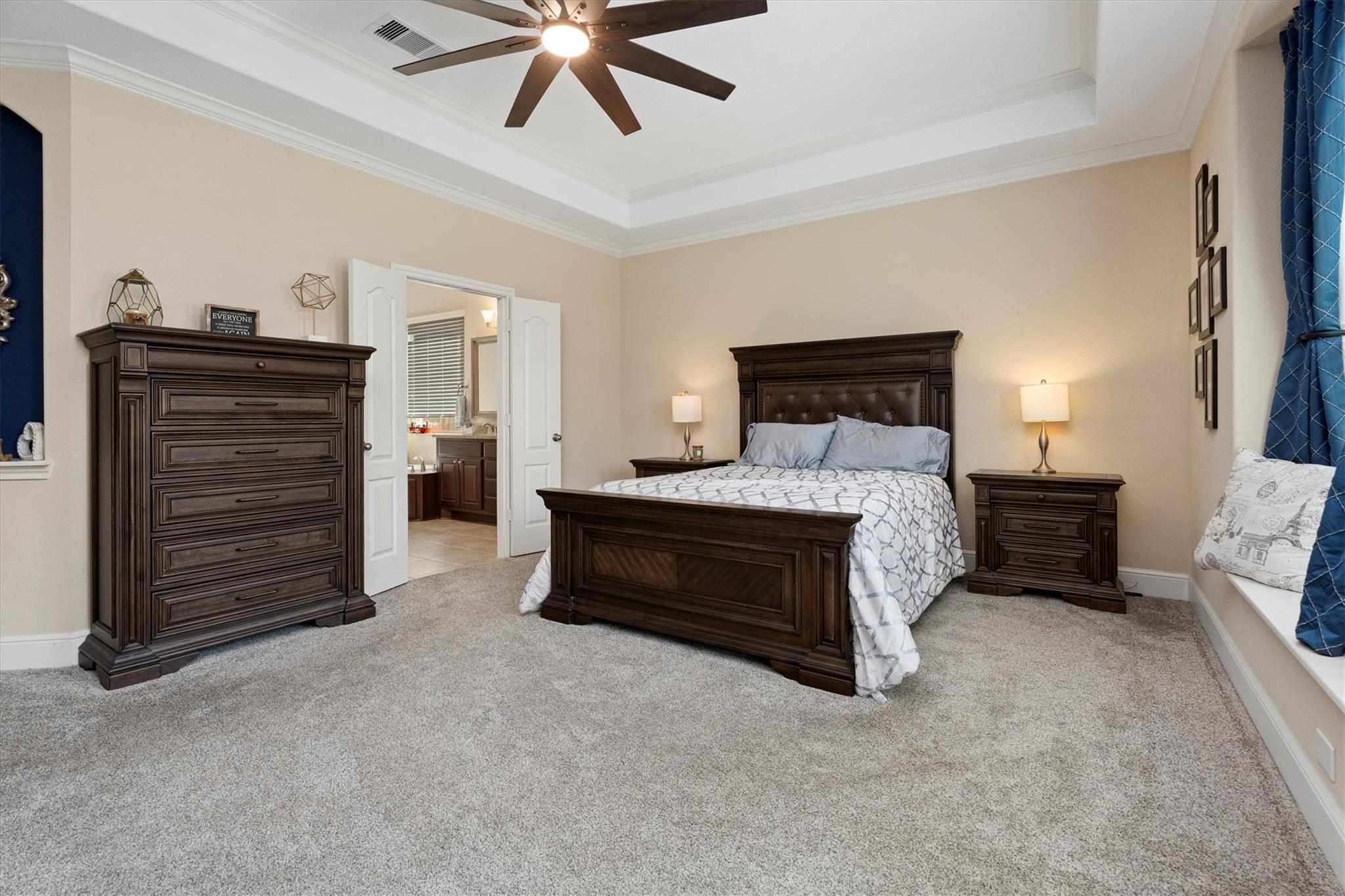 Furnished bedroom with dark wood furniture, gray carpet, and open doors to an adjoining bathroom.