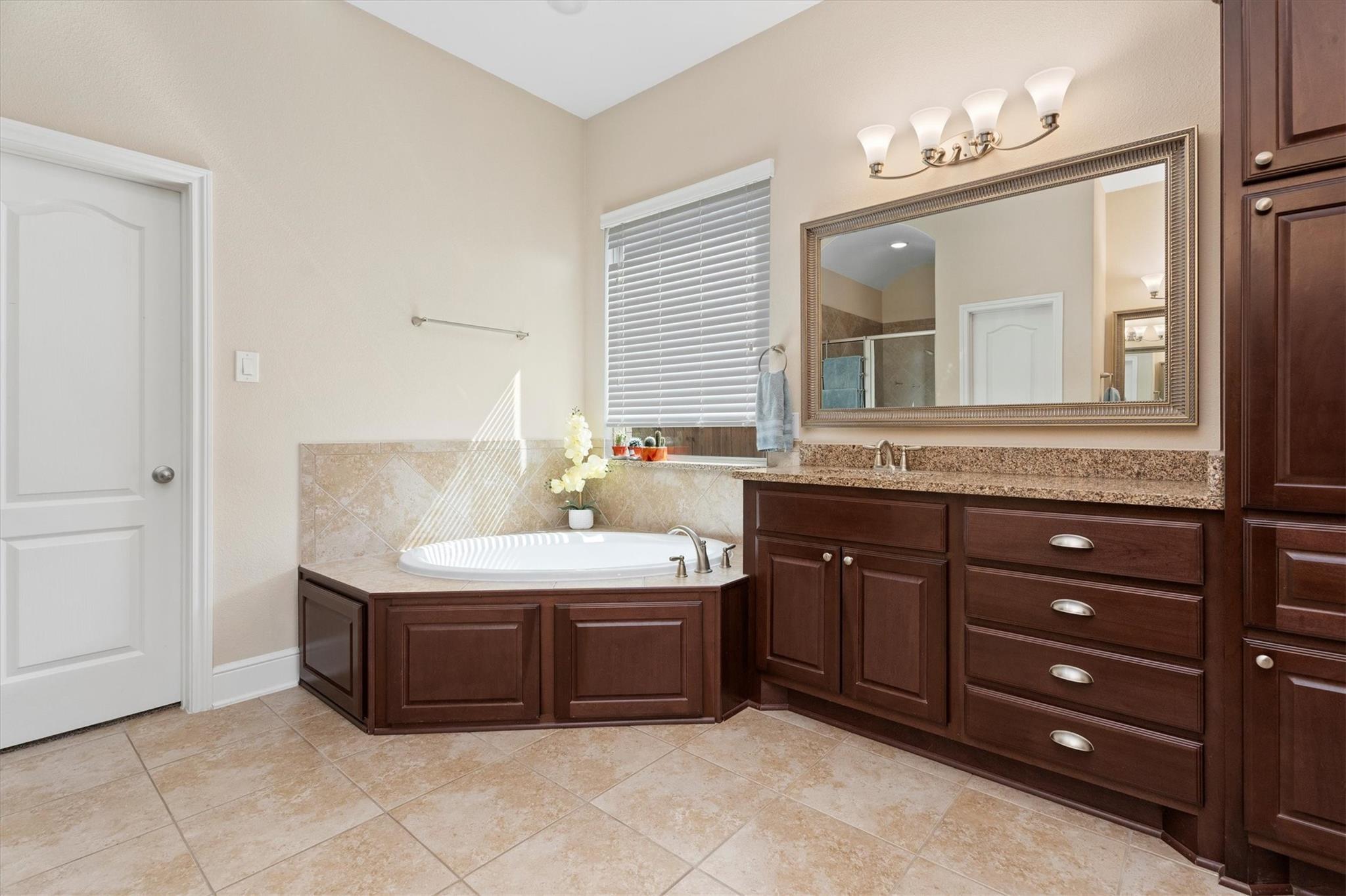 Bathroom with a corner soaking tub, dark wood cabinets, and a long granite vanity.