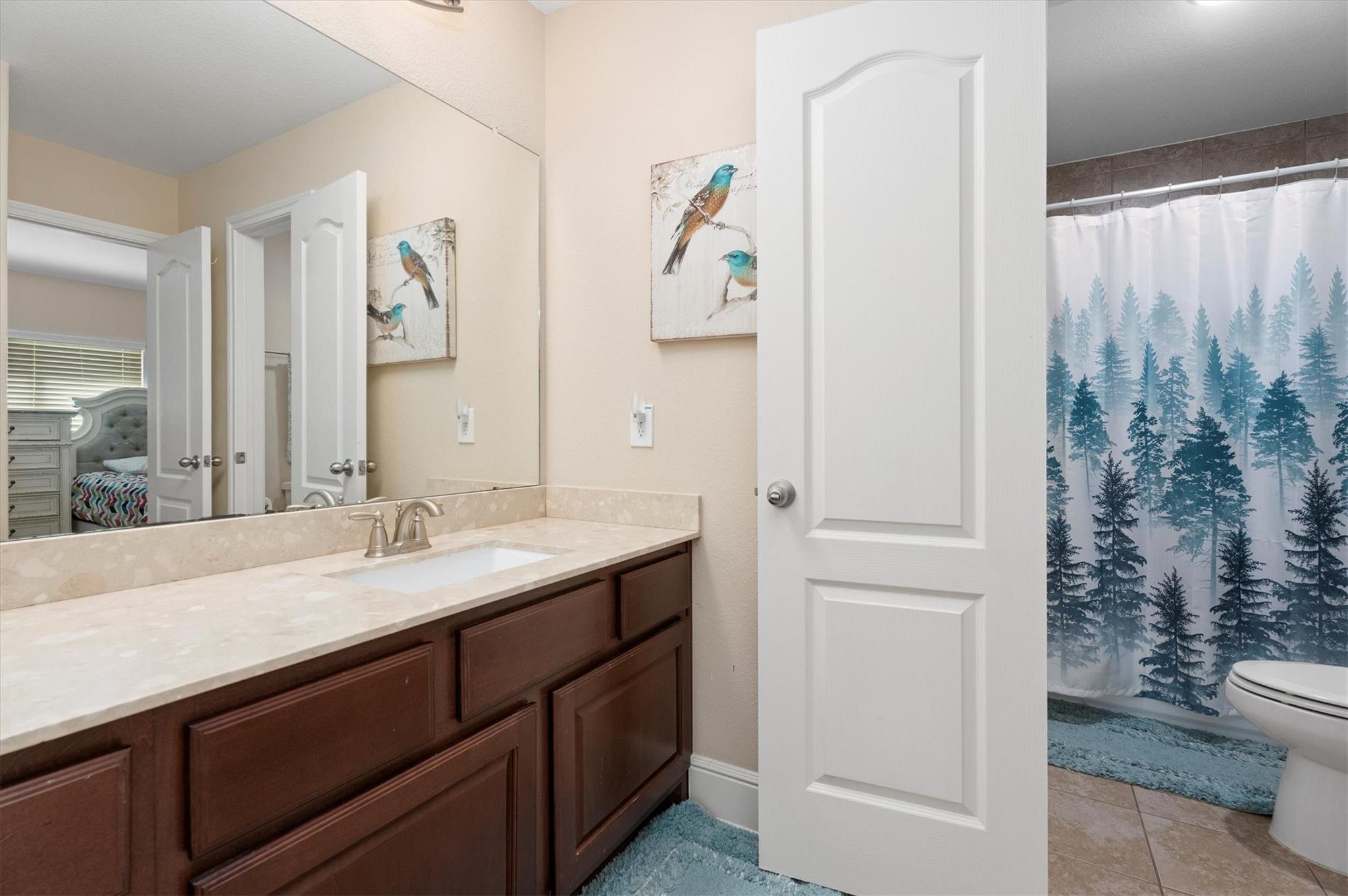 Bathroom with a dark wood vanity, stone countertop, large mirror, and blue forest-print shower curtain.