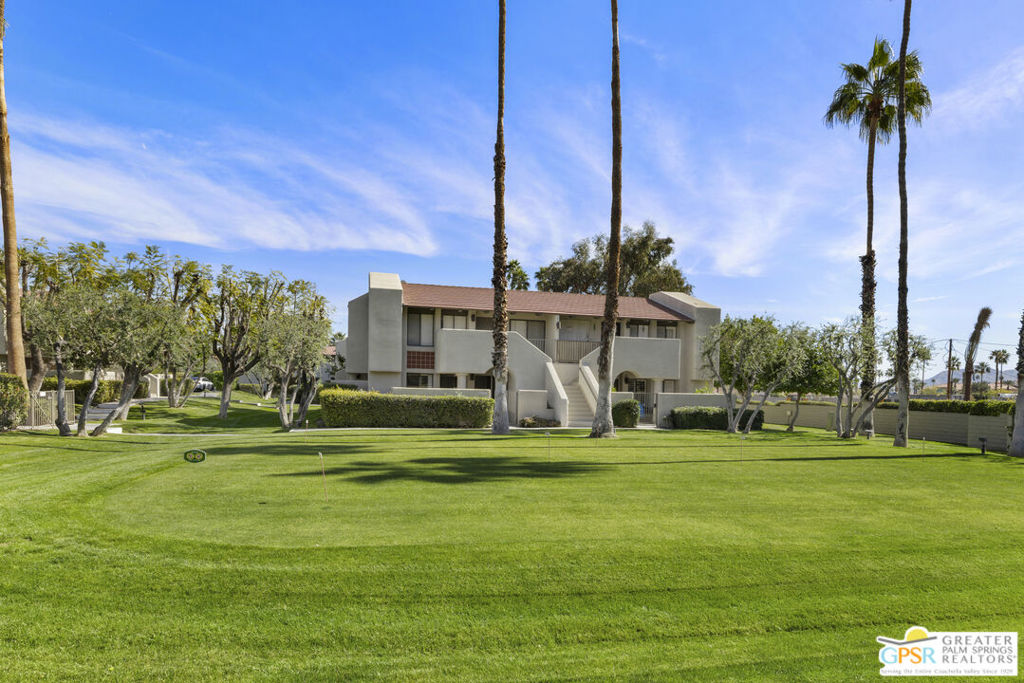 Two-story condominium building beyond a manicured lawn with putting-green holes and palm trees.