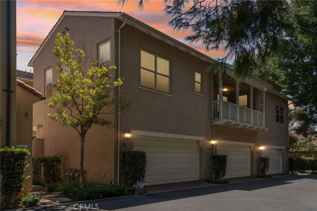 Two-story attached home with a second-floor balcony and three garage doors beneath a pink dusk sky.