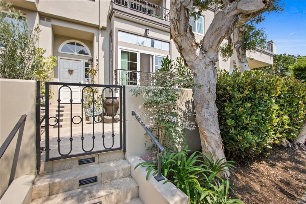 Gated townhouse entry with stone steps, a white front door, and a large tree.