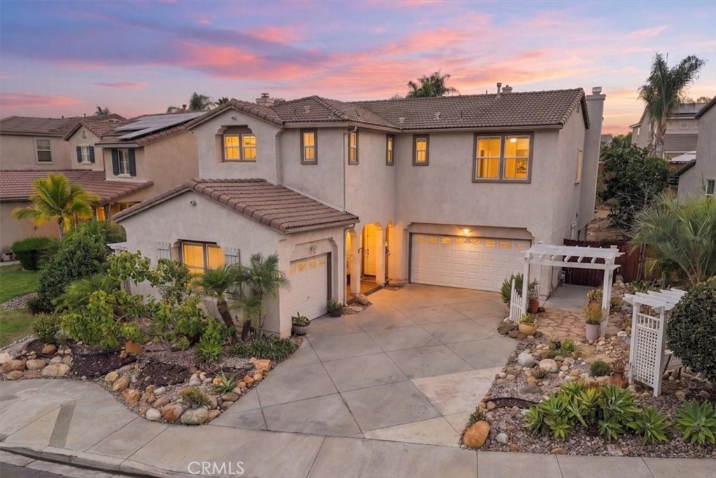 Two-story stucco home with lit windows, attached garages, and landscaped rock gardens at dusk.
