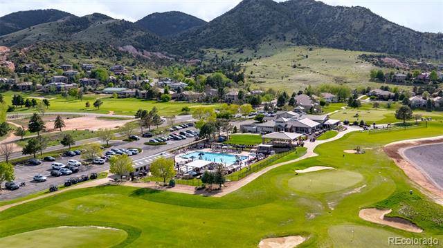 Aerial view of a golf course with a clubhouse, swimming pool, and mountain backdrop.
