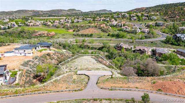 Vacant residential lot outlined beside a paved road, with homes and rolling hills beyond.