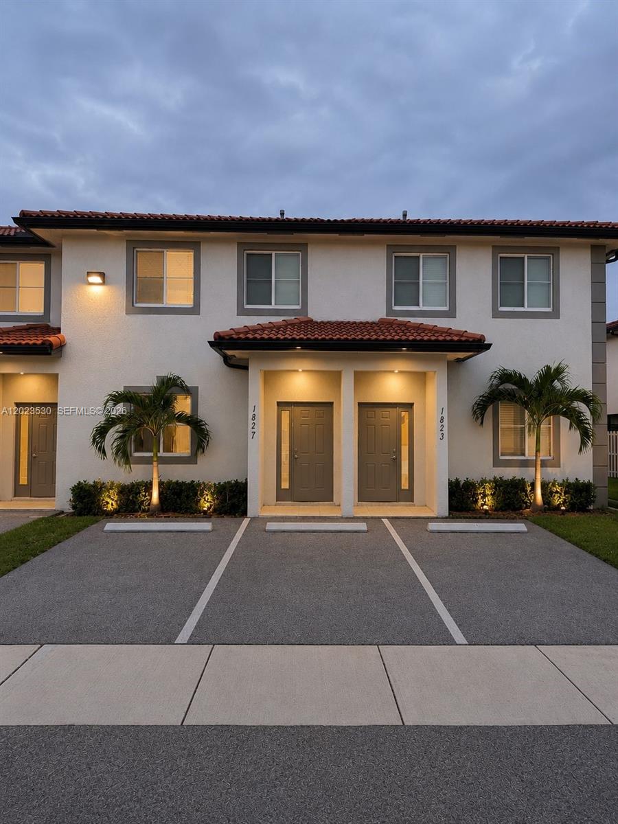 Two-story townhouse facade with paired entries, red tile awnings, and illuminated landscaping at dusk.