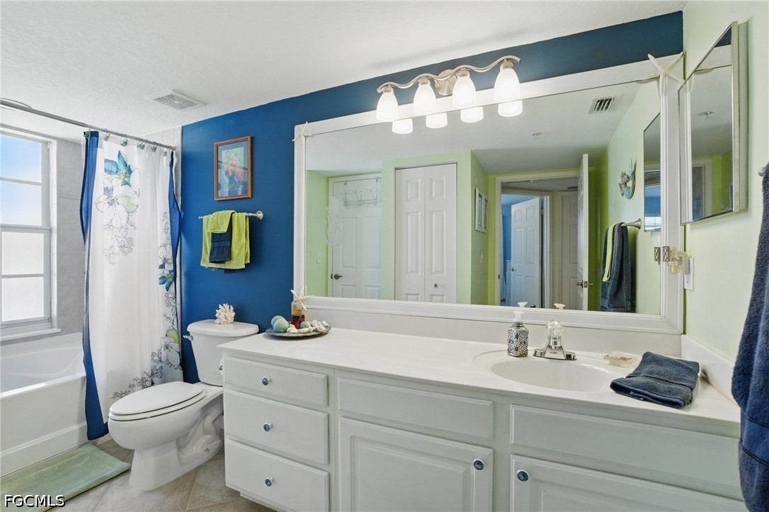 Bathroom with a long white vanity, wall-to-wall mirror, and bathtub behind a floral shower curtain.