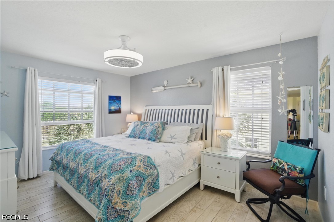 Bedroom with a white bed, blue patterned bedding, two bright windows, and a white nightstand.
