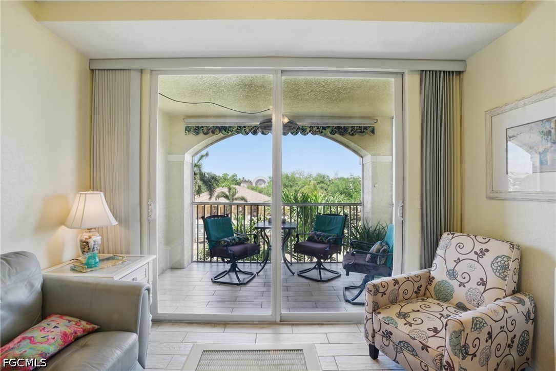 Living room with sliding glass doors opening to a covered balcony with seating and leafy views.