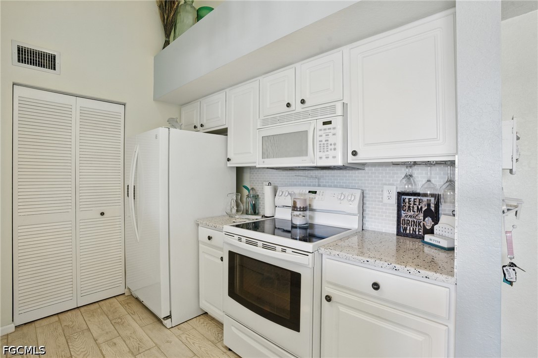 Kitchen with white cabinetry, white appliances, speckled counters, and a light tile backsplash.