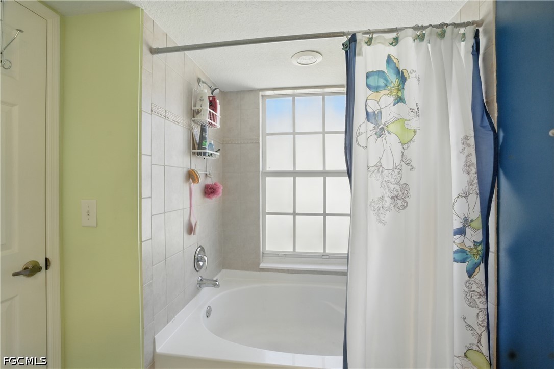 Bathroom with a white bathtub beneath a large window and a floral shower curtain.