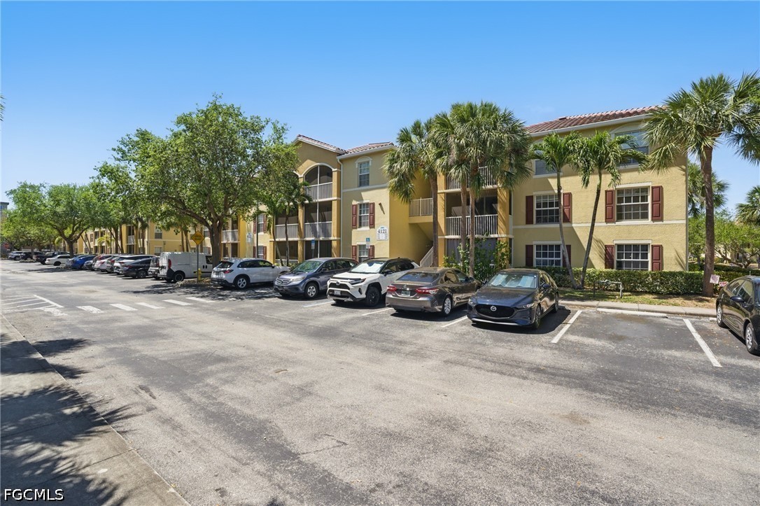 Three-story tan residence with balconies and red shutters beside a palm-lined parking lot.