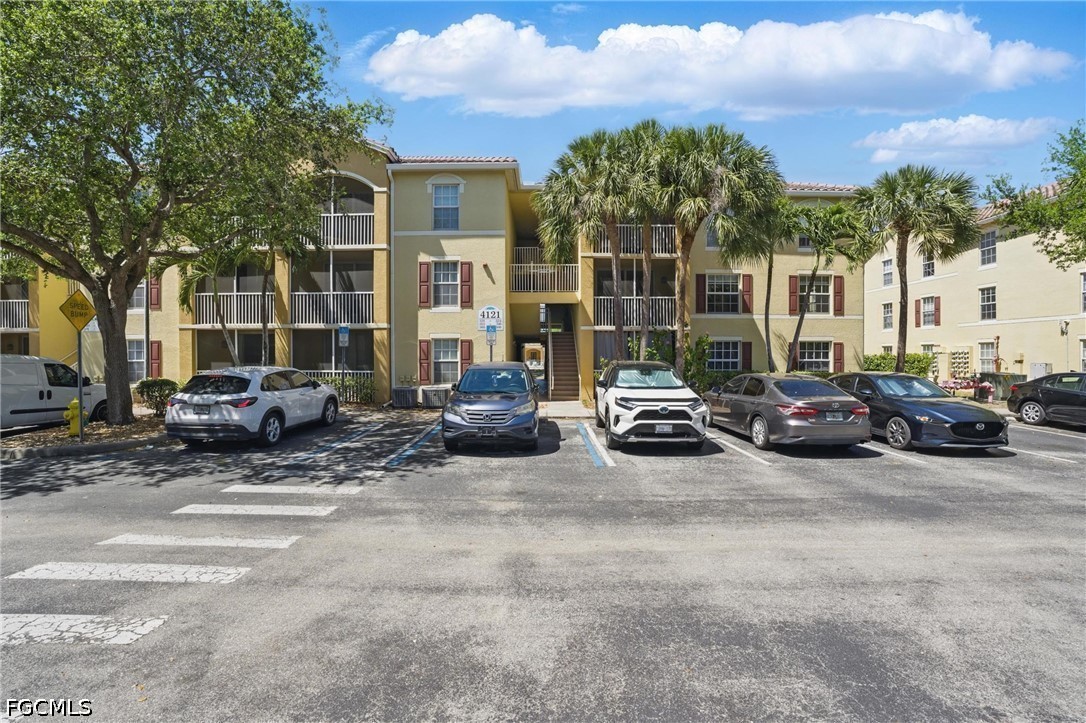 Three-story condominium exterior with balconies, palm trees, and cars parked in front.