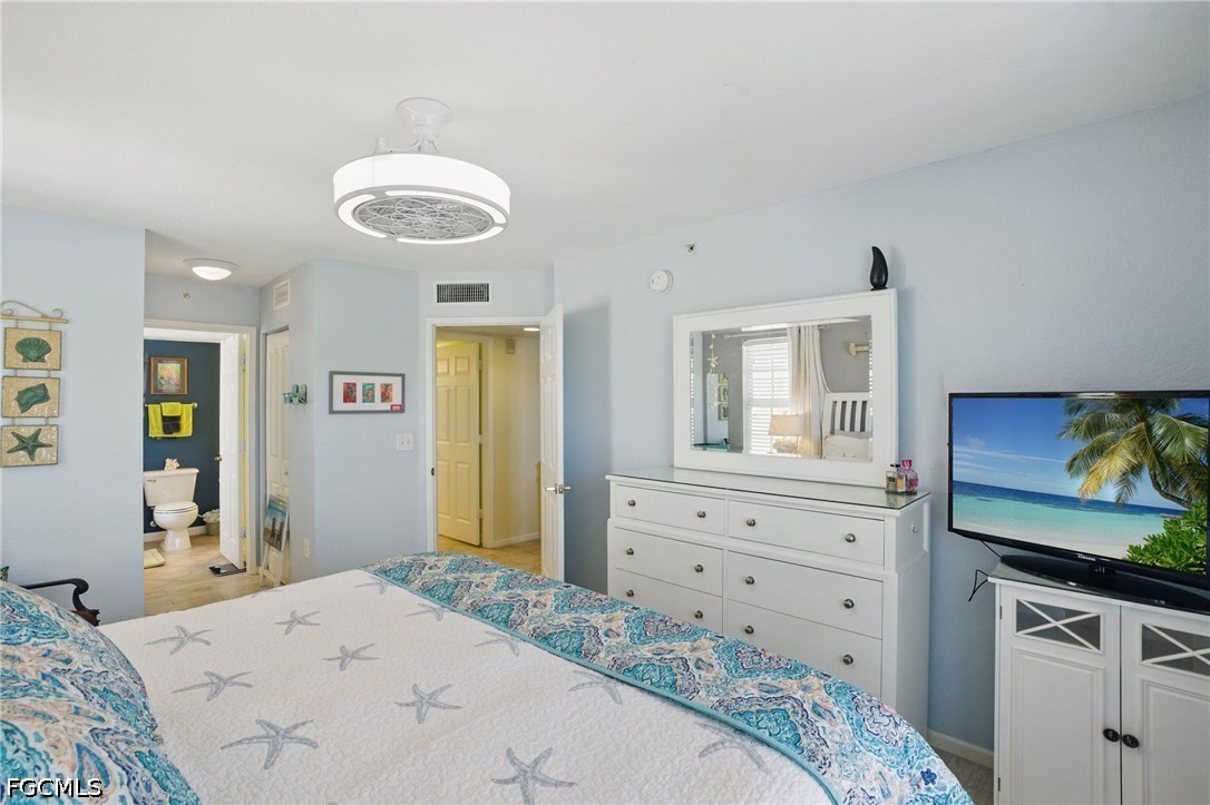 Bedroom with a starfish-patterned bedspread, white dresser, and television showing a tropical beach.