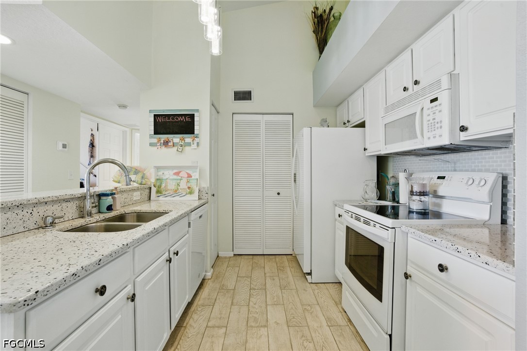 Galley kitchen with white cabinets, speckled counters, and pale wood-look flooring.