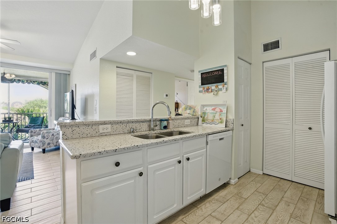 Condo kitchen with white cabinets, speckled countertops, and a sink, opening to a furnished living area and balcony.