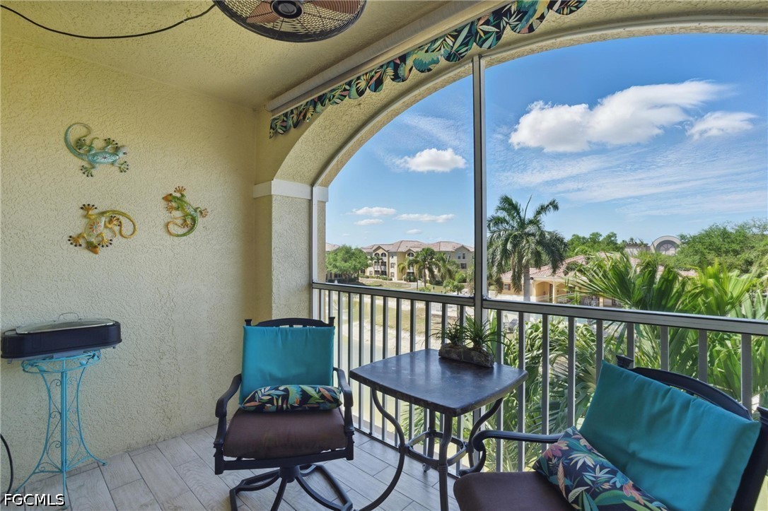 Covered balcony with turquoise-cushioned chairs and a view of palm trees and nearby homes.