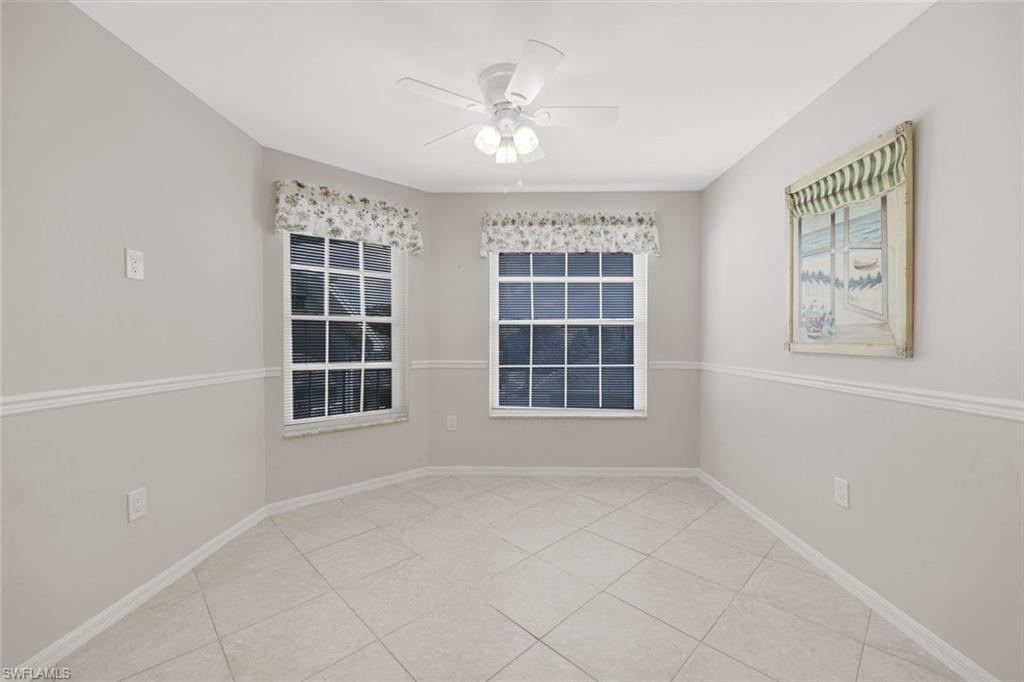 Empty tiled room with two windows, floral valances, and a ceiling fan.