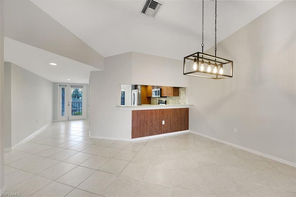 Vacant open-plan living and dining area with tiled floors, vaulted ceiling, and a wood-cabinet kitchen.